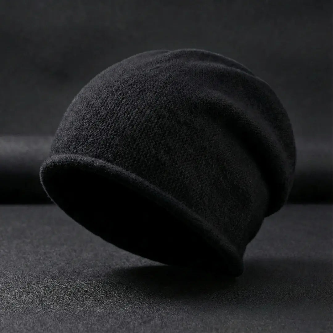 Dark gray beanie on a textured black surface with a dark background
