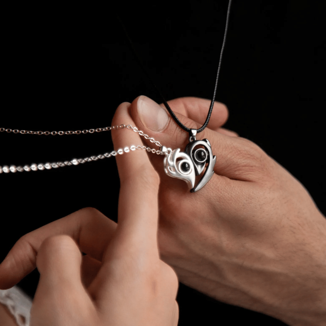 Heart-shaped pendant with owl design held by a hand against a black background