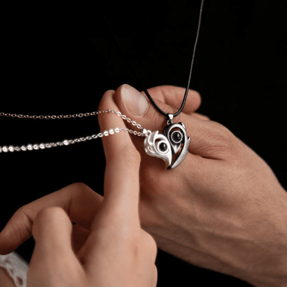 Heart-shaped pendant with owl design held by a hand against a black background
