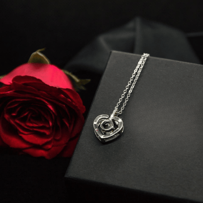 Silver heart-shaped necklace on a black box with a red rose next to it