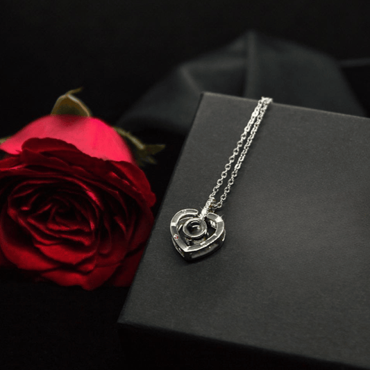 Silver heart-shaped necklace on a black box with a red rose next to it