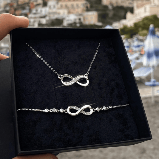 Silver infinity necklace and bracelet set in a black box with a blurred outdoor background.