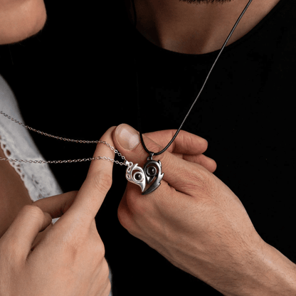 Close-up of two people holding a silver heart-shaped necklace with an owl design.