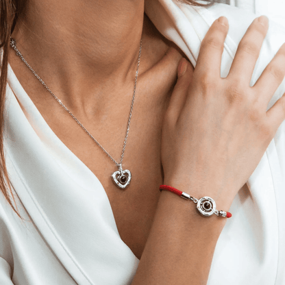 Close-up of a person wearing a silver necklace and bracelet with a red cord on a white background