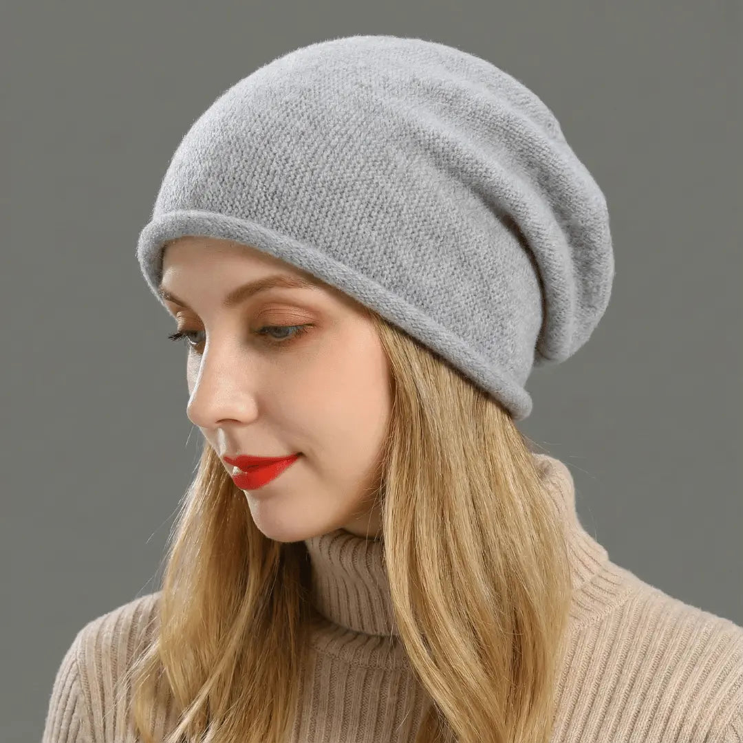 Woman wearing a gray knit beanie and beige turtleneck against a gray background