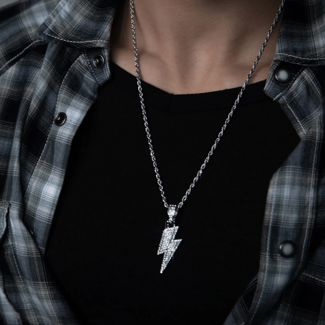 Person wearing a black shirt and plaid jacket with a silver lightning bolt necklace.