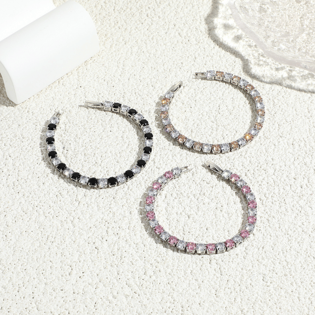 Three hoop earrings with different colorstone accents on a textured white surface