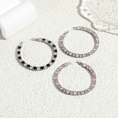 Three hoop earrings with different colorstone accents on a textured white surface