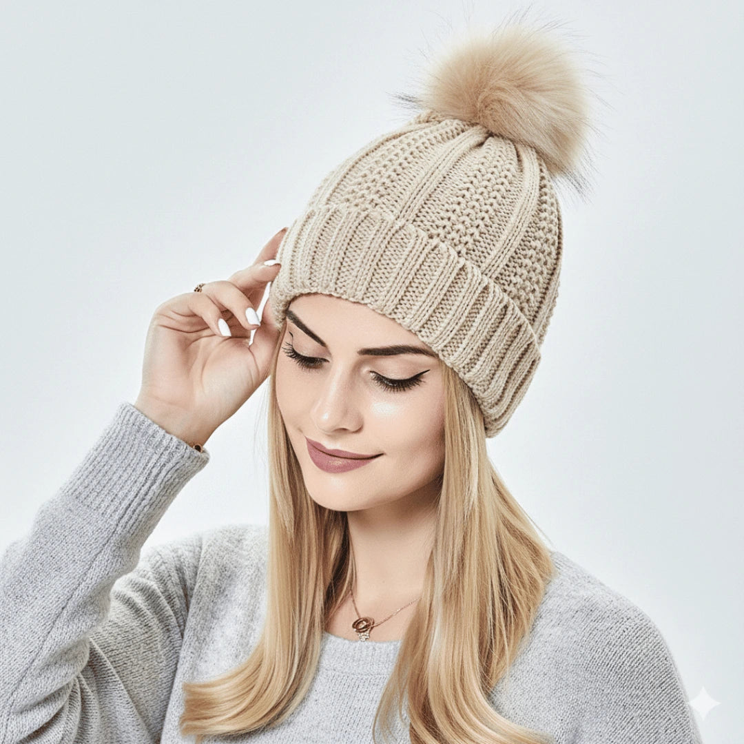 Woman wearing a beige knitted beanie with a fur pom-pom on a light gray background