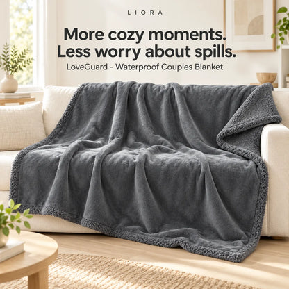 A dark gray fleece blanket draped over a cream sofa in a bright living room, with overlaid text reading 'More cozy moments. Less worry about spills.