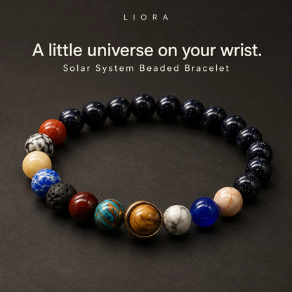 A beaded bracelet arranged in a circle on a dark background, featuring mostly black beads with several accent beads in red, cream, blue, brown, and white, plus a central gold-toned sun-like bead.